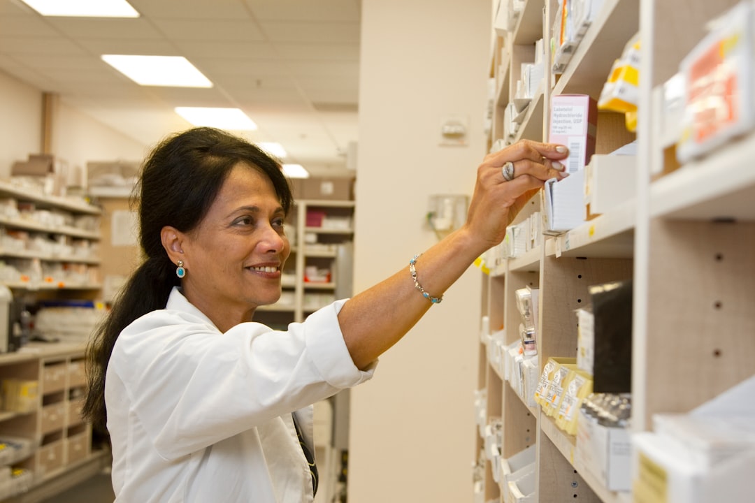 A pharmacist in a white coat reaching for a medication box on a shelf